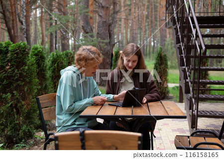 computer awareness of the elderly. a happy teenage girl teaches older 70s grandmothers to use a laptop at home. social media and modern technologies 116158165