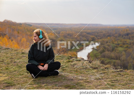 Young woman relaxing on a bench on seafront promenade with her mobile phone and music on her headphones browsing a tune with a smile 116158292