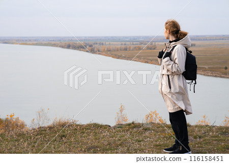 A young girl stands on a high bank and looks at the beautiful nature 116158451