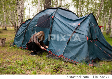 A woman sets up a tent in the forest 116158577
