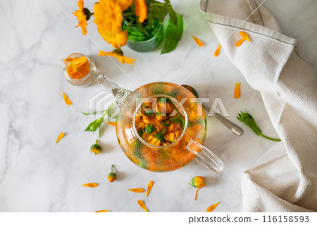 Cup of marigold tea and calendula flowers outdoors on green background. Cup of marigold tea and calendula flowers outdoors on green background. 116158593