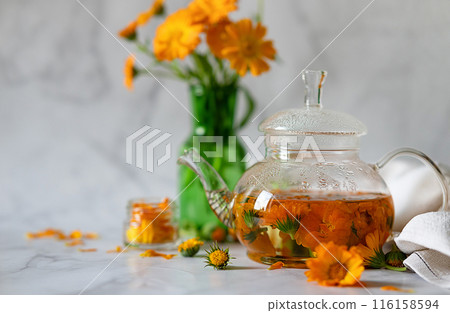 Cup of marigold tea and calendula flowers outdoors on green background. Cup of marigold tea and calendula flowers outdoors on green background. 116158594