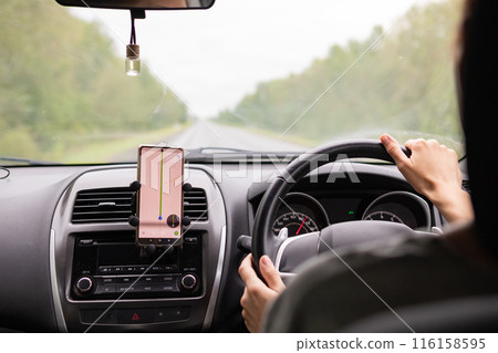 Rear view of a young traveler using a navigator on a mobile phone behind the wheel of a modern car . 116158595