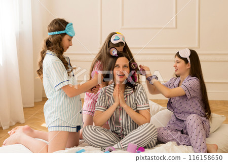 Girls and mom enjoy playful hairstyling in pajamas. 116158650