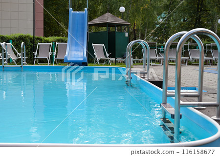 Shiny stainless steel swimming pool handrails next to the blue swimming pool The edge of the pool floor is covered with smart boards. There are many beds and pool chairs. Shiny stainless steel swimming pool handrails next to the blue swimming pool The edge of the pool floor is covered with smart boards. There are many beds and pool chairs. 116158677