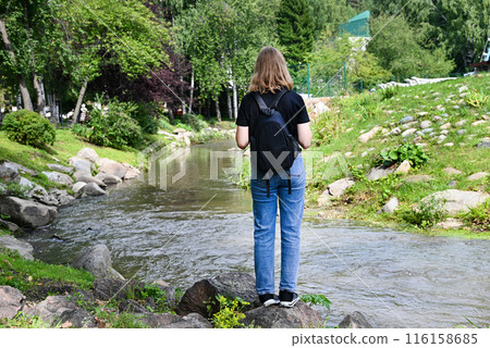A young lady is sitting on large rocks next to a mountain river. A young lady is sitting on large rocks next to a mountain river. 116158685