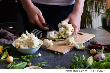 A woman cuts fresh cauliflower at the table A woman cuts fresh cauliflower at the table 116158750