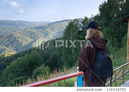 View from the back of young hiker girl wearing backpack and beanie hat standing on edge of cliff and enjoying landscape, sunset, mountains and clouds. View from the back of young hiker girl wearing backpack and beanie hat standing on edge of cliff and enjoying landscape, sunset, mountains and clouds. 116158785