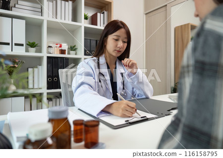 Female Doctor Consulting Patient in Modern Medical Office with Shelves and Medicine Bottles Female Doctor Consulting Patient in Modern Medical Office with Shelves and Medicine Bottles 116158795