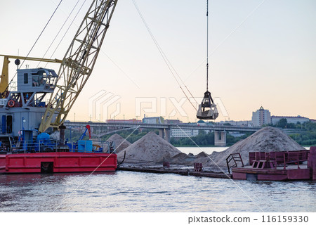 River port. Port cranes on the river bank. Extraction and transportation of sand and other goods. The embankment of the river port, a barge at the mooring wall. 116159330
