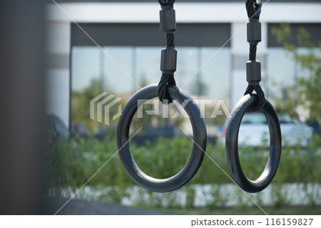 Gymnastic rings to strengthen the arms on street sport ground. Outdoor sports field. Healthy lifestyle. Close up. Gymnastic rings to strengthen the arms on street sport ground. Outdoor sports field. Healthy lifestyle. Close up. 116159827