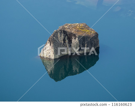 Huge boulder in the lake, stone reflection in still clear blue water. 116160623