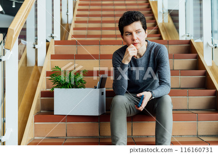 Stressed worried middle aged gender neutral woman with box of personal items sitting alone on the staircase after being fired, lost job due to recession and economic stress. Equality discrimination. Stressed worried middle aged gender neutral woman with box of personal items sitting alone on the staircase after being fired, lost job due to recession and economic stress. Equality discrimination. 116160731