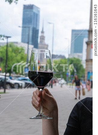 Red wine glass in hand on blurred Warsaw cityscape background. Wineglasses dinner on restaurant terrace 116161643