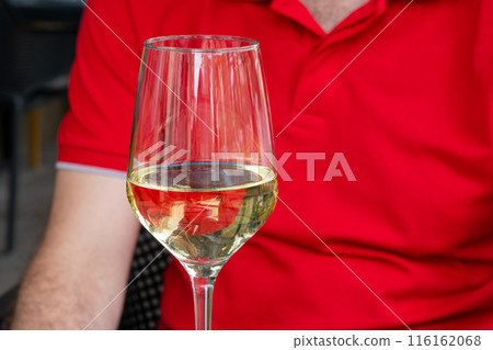 White wine glass on red background closeup. Mans hand holding a glass of white wine, summer relaxing outdoors White wine glass on red background closeup. Mans hand holding a glass of white wine, summer relaxing outdoors 116162068