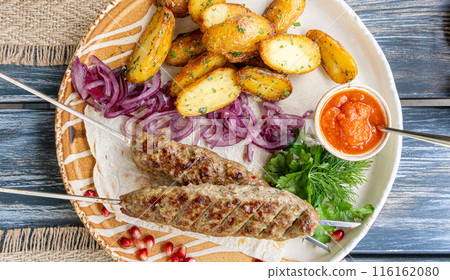 Georgian lula kebab with baked potatoes, sauce and greens. Grilled souvlaki, minced meat kebap, lamb on skewers Georgian lula kebab with baked potatoes, sauce and greens. Grilled souvlaki, minced meat kebap, lamb on skewers 116162080