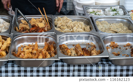 Assorted Asian street food in stainless steel trays, fried squid, various dumplings, spring rolls at food market Assorted Asian street food in stainless steel trays, fried squid, various dumplings, spring rolls at food market 116162123
