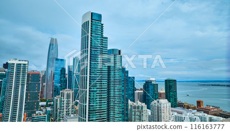 San Francisco skyscrapers in wall of blue windows with boat on bay water in aerial, CA 116163777