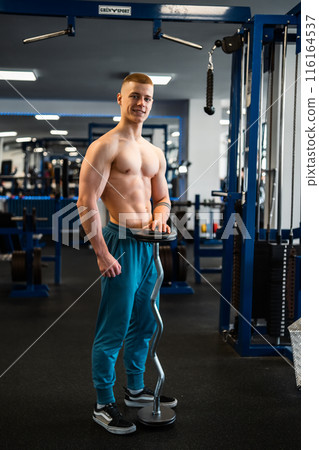 Young fitness trainer holding a barbell standing in the gym.  116164537