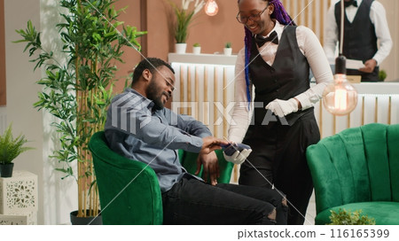 Guest paying for cup of coffee to hotel staff, using card at pos while he waits for room registration. African american traveller paying for drink, discussing with receptionist about services. 116165399