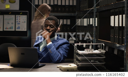 Focused african american detective investigates evidence and analyzes clues while caucasian inspector does research. Black policeman sitting with laptop to solve complex cases and uphold justice. 116165402