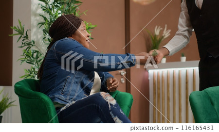 Traveller gives cash money to bellboy, paying for cup of coffee received from hotel cafeteria. African american woman providing tips to concierge staff, excellent service. Handheld shot. 116165431