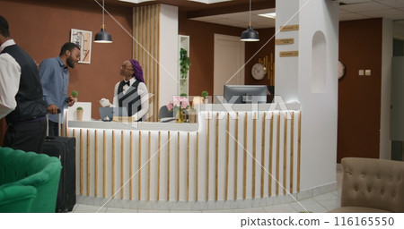 Hotel guest getting room access card after check in procedure at reception entrance, meeting with front desk employee asking about services. African american man travelling on vacation. Hotel guest getting room access card after check in procedure at reception entrance, meeting with front desk employee asking about services. African american man travelling on vacation. 116165550