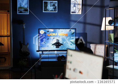 Happy gamer celebrating shooting contest victory, playing video games on television in the living room. Adult feeling joyful after winning online first person tournament, leisure activity. 116165571