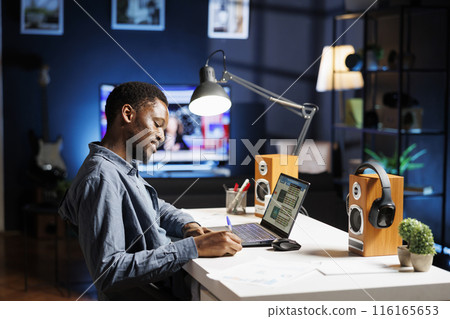 Legal advisor writing adhesive notes for reminders, putting information on post it memo at home. Young adult working on freelance contract, telework tasks from his workstation. 116165653