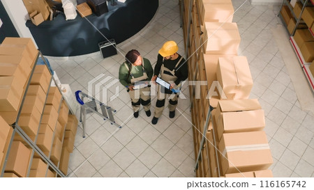 Jib up shot of warehouse sorters comparing findings after finishing inspecting cardboard box parcels. Production technicians making sure stocks and inventory are well organized Jib up shot of warehouse sorters comparing findings after finishing inspecting cardboard box parcels. Production technicians making sure stocks and inventory are well organized 116165742