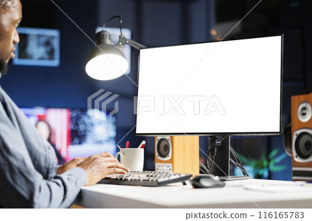 African american man checks white screen on computer, teleworking and using blank display on monitor. Male employee does remote work at home with empty chromakey design at desk. African american man checks white screen on computer, teleworking and using blank display on monitor. Male employee does remote work at home with empty chromakey design at desk. 116165783