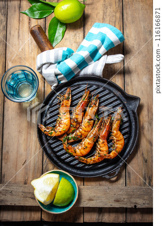 Grilled shrimp on a black grill pan on a rustic wooden table, with limes, a blue-striped cloth Grilled shrimp on a black grill pan on a rustic wooden table, with limes, a blue-striped cloth 116166871