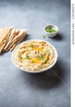 Bowl of creamy hummus garnished with olive oil and herbs is served with pita bread on a wooden board. A small bowl of garnish is placed beside the bread on a slate surface Bowl of creamy hummus garnished with olive oil and herbs is served with pita bread on a wooden board. A small bowl of garnish is placed beside the bread on a slate surface 116166875