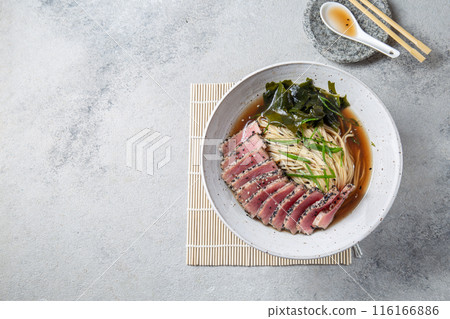 A bowl of ramen featuring perfectly seared tuna slices, garnished with fresh greens, seaweed, and served in a savory broth. 116166886