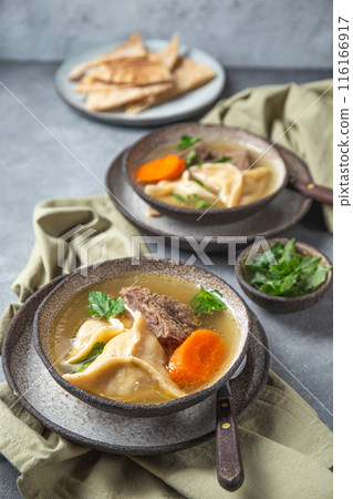 Traditional Jewish Kreplach soup with meat and carrot, gray background Traditional Jewish Kreplach soup with meat and carrot, gray background 116166917