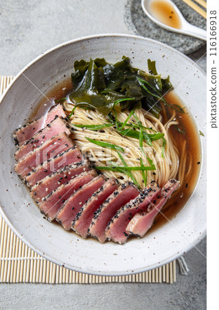 A bowl of ramen featuring perfectly seared tuna slices, garnished with fresh greens, seaweed, and served in a savory broth. A bowl of ramen featuring perfectly seared tuna slices, garnished with fresh greens, seaweed, and served in a savory broth. 116166918