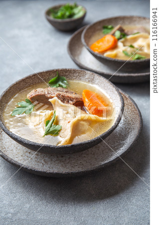 Traditional Jewish Kreplach soup with meat and carrot, gray background Traditional Jewish Kreplach soup with meat and carrot, gray background 116166941