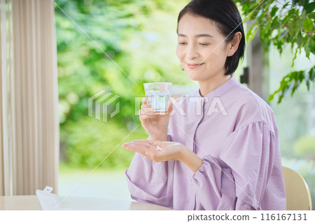 Smiling middle-aged woman taking medicine in the living room Smiling middle-aged woman taking medicine in the living room 116167131