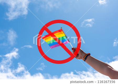 LGBTQ rainbow flag held against a blue sky with a prohibition sign. Concept of canceling a gay or pride event 116167356