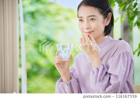 Smiling middle-aged woman taking medicine in the living room 116167359