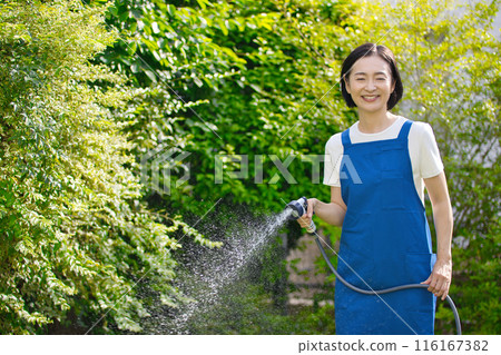 A smiling middle-aged woman watering the greenery in her garden 116167382