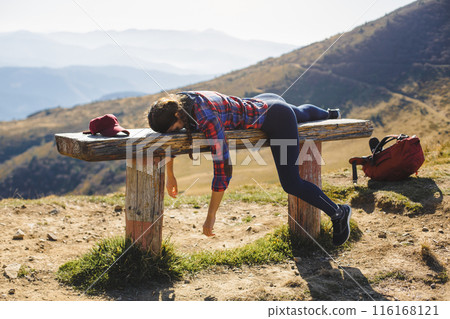 Exhausted Hiker Sprawled on Wooden Bench in Mountain Scenery 116168121