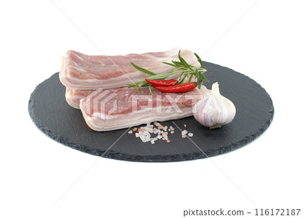 Raw pork belly slices with garlic and chili peppers on a black stone plate Raw pork belly slices with garlic and chili peppers on a black stone plate 116172187