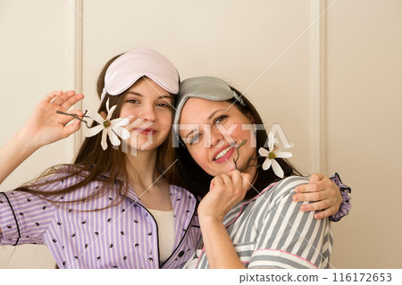 Mother and daughter in pajamas holding flowers and smiling. 116172653