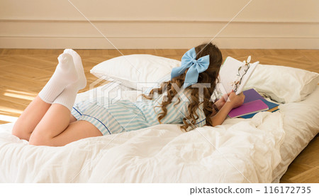 Young girl with blue hair bow reading book 116172735