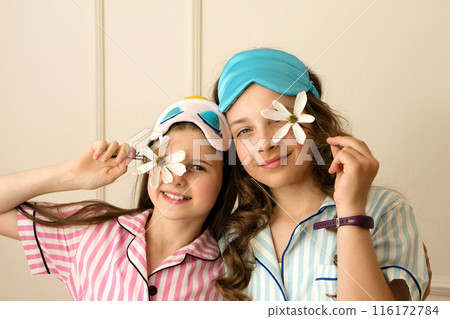 Girls in pajamas holding flowers up to eyes. 116172784