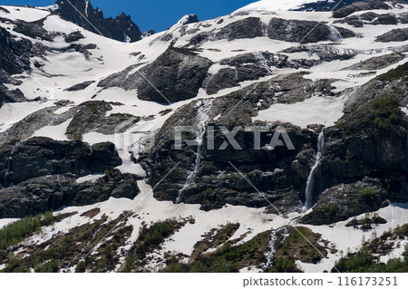 Snow-covered rocky mountain slopes with multiple waterfalls Snow-covered rocky mountain slopes with multiple waterfalls 116173251