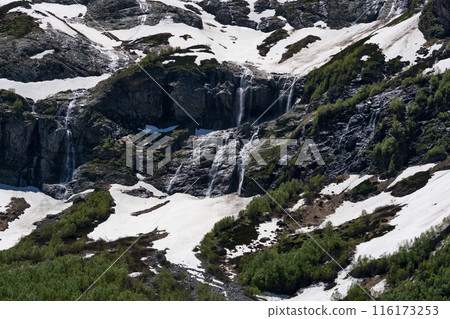 Snowy mountains with cascading waterfalls and green vegetation 116173253