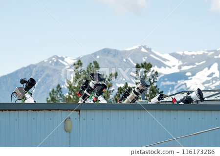 Telescopes on rooftop with mountains in background. Telescopes on rooftop with mountains in background. 116173286