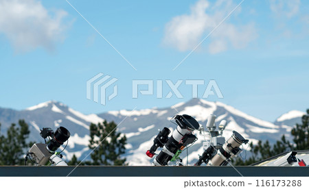 Telescopes on rooftop with snow-covered mountains in background. Telescopes on rooftop with snow-covered mountains in background. 116173288